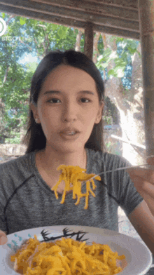 a woman is eating yellow noodles with a fork from a bowl