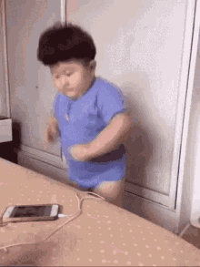 a little boy in a blue shirt is dancing on a bed next to a cell phone .