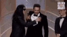 a man in a tuxedo is being helped by another man in a tuxedo at the golden globe awards .
