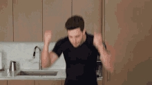 a man in a black shirt is dancing in front of a kitchen sink