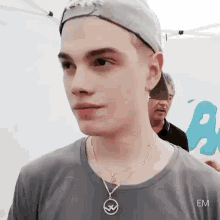 a young man wearing a baseball cap and a necklace is standing in front of a tent .