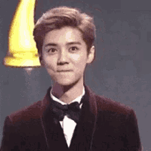 a young man wearing a suit and bow tie is making a funny face .