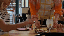 a woman in an apron is serving a glass of lemonade to another woman