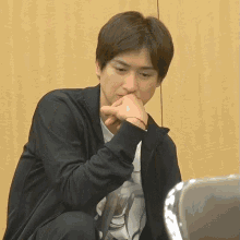 a man in a black jacket sits with his hands on his face