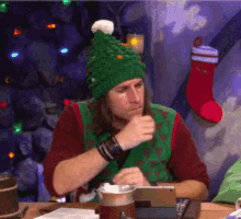 a man wearing a green hat and a green sweater looks at a tablet