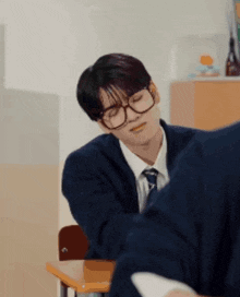 a man wearing glasses and a tie is sitting at a desk in a classroom .