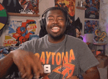 a man wearing headphones and a daytona shirt smiles