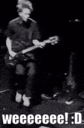 a man is playing a guitar on a stage in a black and white photo with the words weeeee ! : d .