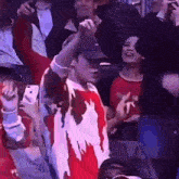 a man wearing a hat and a red and white sweater is cheering in a crowd .