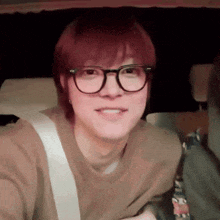 a young man wearing glasses and a brown shirt smiles for the camera