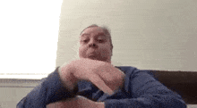 a man in a blue shirt is sitting on a couch and making a funny face with his hands .