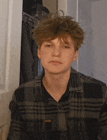 a young man wearing a plaid shirt is standing in front of a door