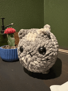 a stuffed animal with black eyes sits on a table next to a potted plant