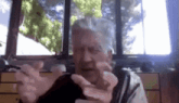 a man with gray hair is sitting in front of a window and making a funny face .