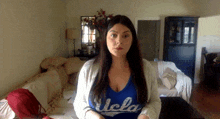 a woman wearing a blue ucla shirt is standing in a living room