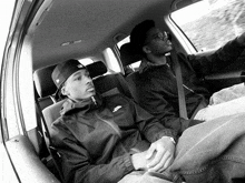two young men are sitting in the back seat of a car one is wearing a jacket that says the north face