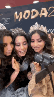 three women wearing tiaras are posing for a photo in front of a sign that says moda2