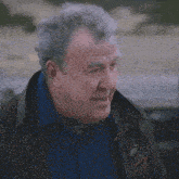 a man with gray hair and a blue shirt is wearing a brown jacket