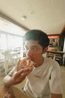 a man wearing a white shirt with 2002 on the front is eating a slice of pizza