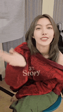 a woman wearing a red shirt that says story is sitting on a stool