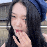 a woman with long black hair wearing a blue hat covering her mouth with her hand