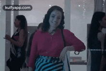 a woman in a pink shirt and striped skirt is smiling while standing in a room .