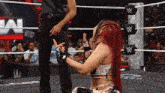 a woman with red hair is kneeling down in a wrestling ring with a referee