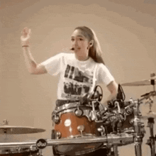 a young girl is playing a drum set and waving at the camera .