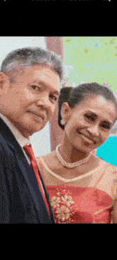 a man and a woman are posing for a picture together . the woman is wearing a pearl necklace .