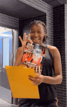 a woman is holding a yellow folder and a magazine in her hands .