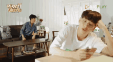 a man is sitting on a couch while another man looks at a cell phone