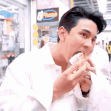 a man in a white shirt is eating a sandwich while talking on a cell phone .
