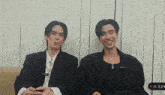 two men are sitting next to each other and one of them is wearing a black jacket