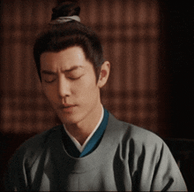 a man with his eyes closed is wearing a kimono and a bun