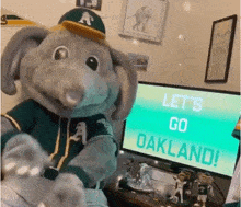 an elephant mascot is standing in front of a computer monitor that says let 's go oakland