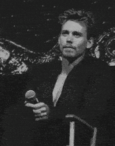 a man in a suit is sitting in a chair holding a microphone and smiling .
