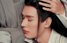 a man with long hair is laying down with his eyes closed and a hand on his head