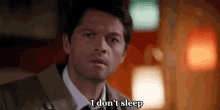 a man in a suit and tie is sitting on a couch and says `` i don 't sleep '' .