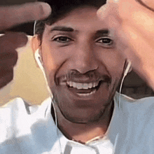 a man wearing ear buds and a white shirt is smiling