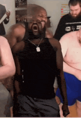 a man in a black tank top with a necklace around his neck stands in a crowd of men