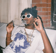 a man wearing sunglasses and a the smiths t-shirt smoking a cigarette