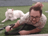 a man with glasses is using a vacuum cleaner while a white dog lays in the background
