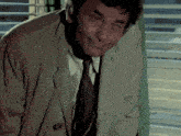 a man in a trench coat and tie is smiling