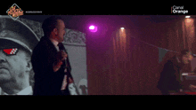 a man singing into a microphone in front of a channel orange sign