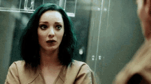 a woman with green hair is standing in front of a mirror looking at herself .