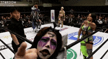 a woman with purple paint on her face is giving a thumbs up in a wrestling ring ..