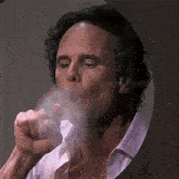 a man in a white shirt smoking a cigarette with smoke coming out of his mouth
