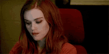 a woman with red hair is sitting in a red chair and looking at the camera .