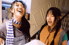 two girls are laughing and one is wearing overalls and a scarf