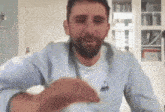 a man with a beard is wearing a light blue sweatshirt with a le coq sportif logo on the front .